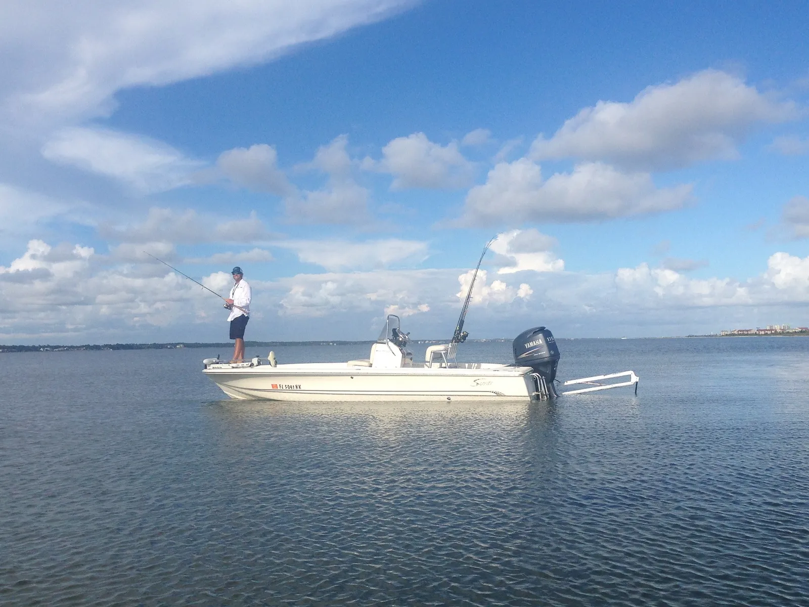 Angler casting from the bow of a white flats boat on calm water under blue skies