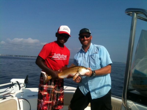 A young angler holding his first redfish next to Captain Mike