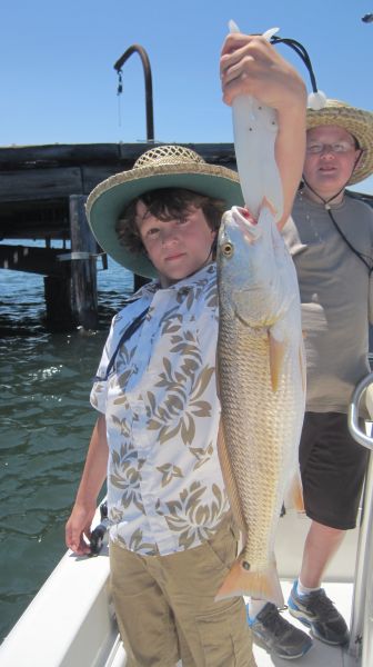 A boy in a straw hat holding up a redfish beside a pier